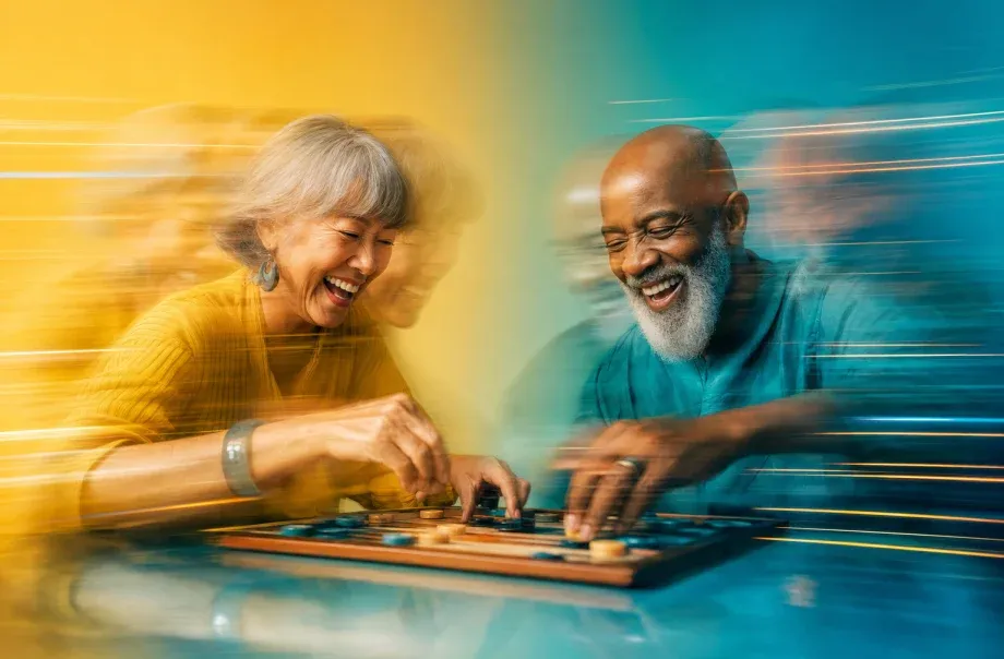 Two adults laughing over a board game at a bright table.
