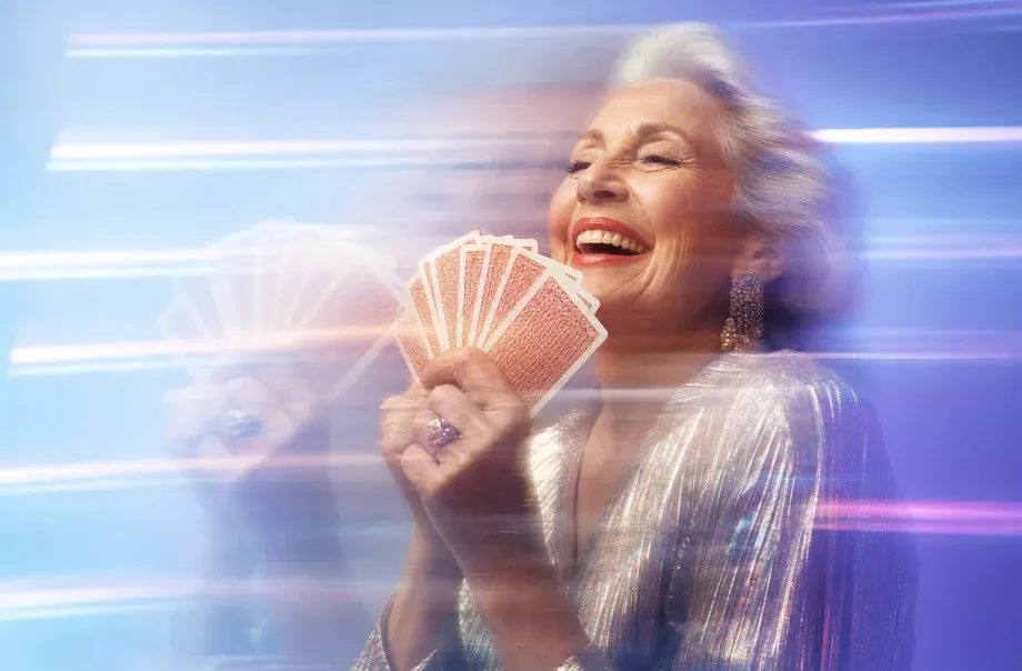 An older woman laughing while holding a hand of playing cards.